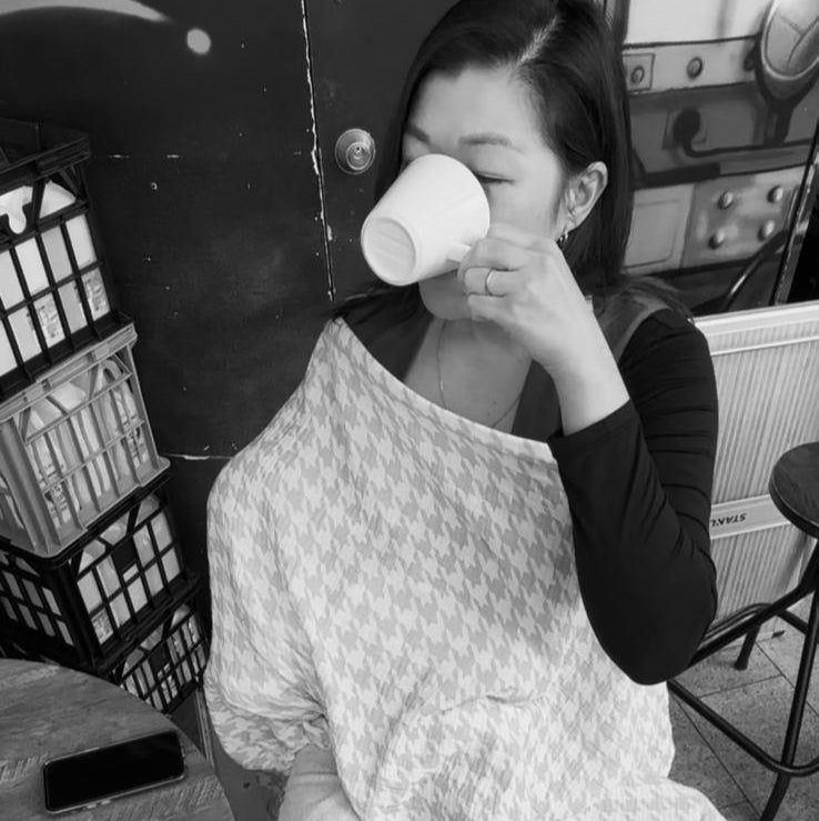 Person sitting at a table in a cafe, holding a cup.